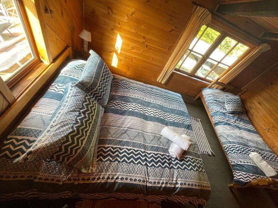 Habitación con cama matrimonial y cama individual, paredes y techo de madera, con ventanas al jardín